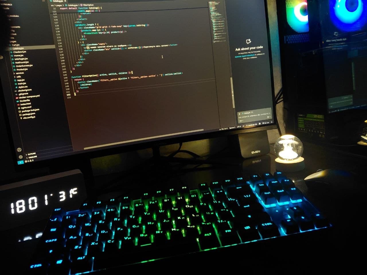 My desk: a monitor with code on the screen, a backlit keyboard, a desk clock and a lamp in a glass globe